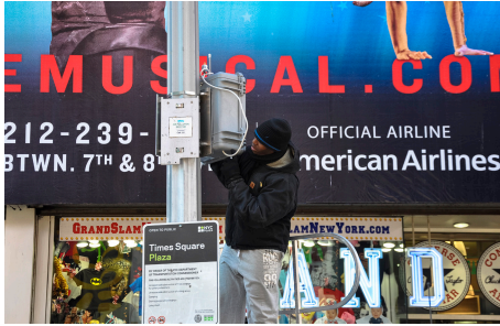 A man places an air survey monitor, which is a small gray box, on a street pole.