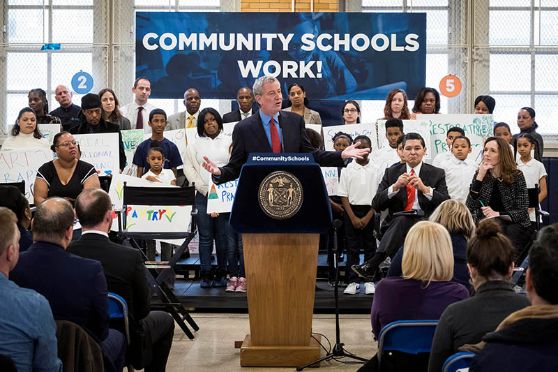 Mayor Bill de Blasio stands at a podium in front of students and teachers