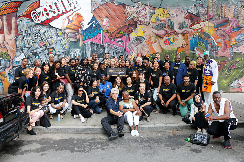 A large group gathering in front of a mural, posing for a picture