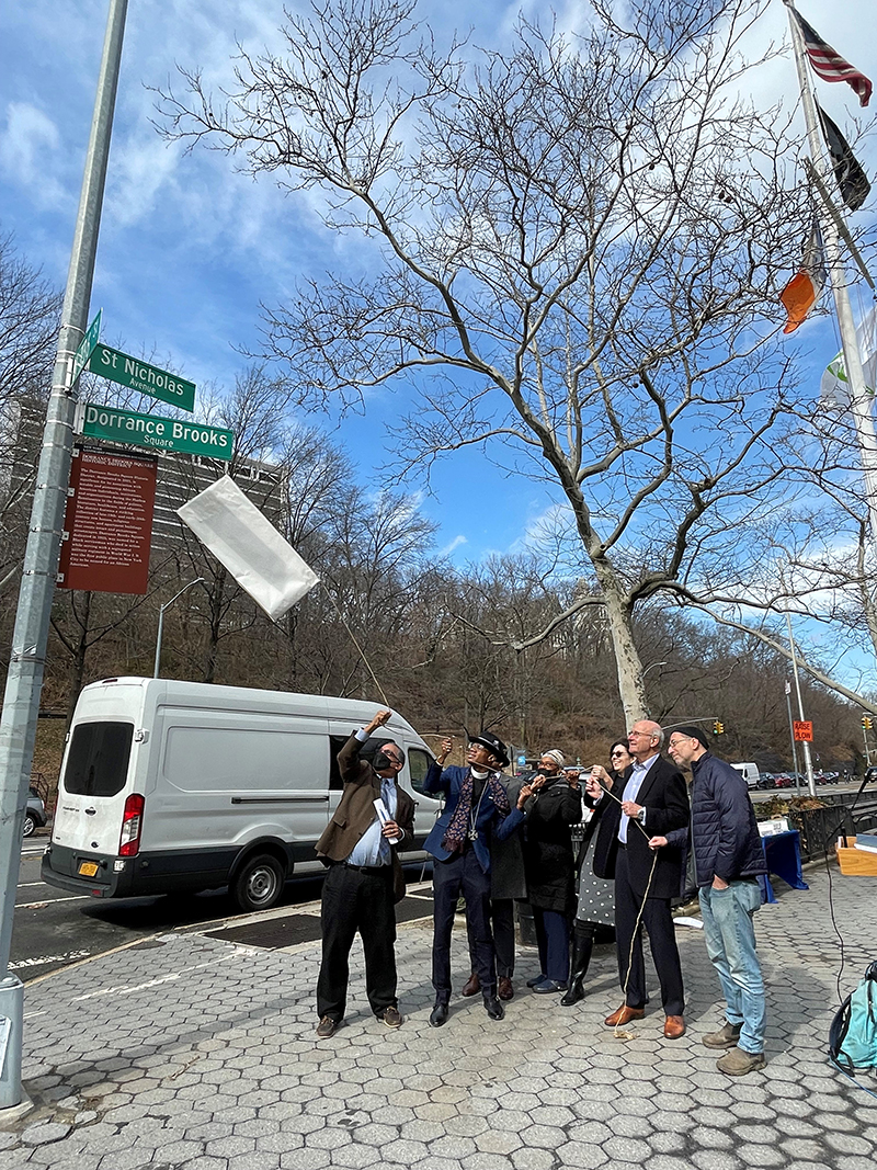 Landmarks Preservation Commission Chair Sarah Carroll, Commissioner Michael Goldblum, Keith Taylor, president of the Dorrance Brooks Property Owners and Residents Association, and members of the community pull the string to remove the paper covering and unveil the new Dorrance Brooks Square Historic District marker sign.