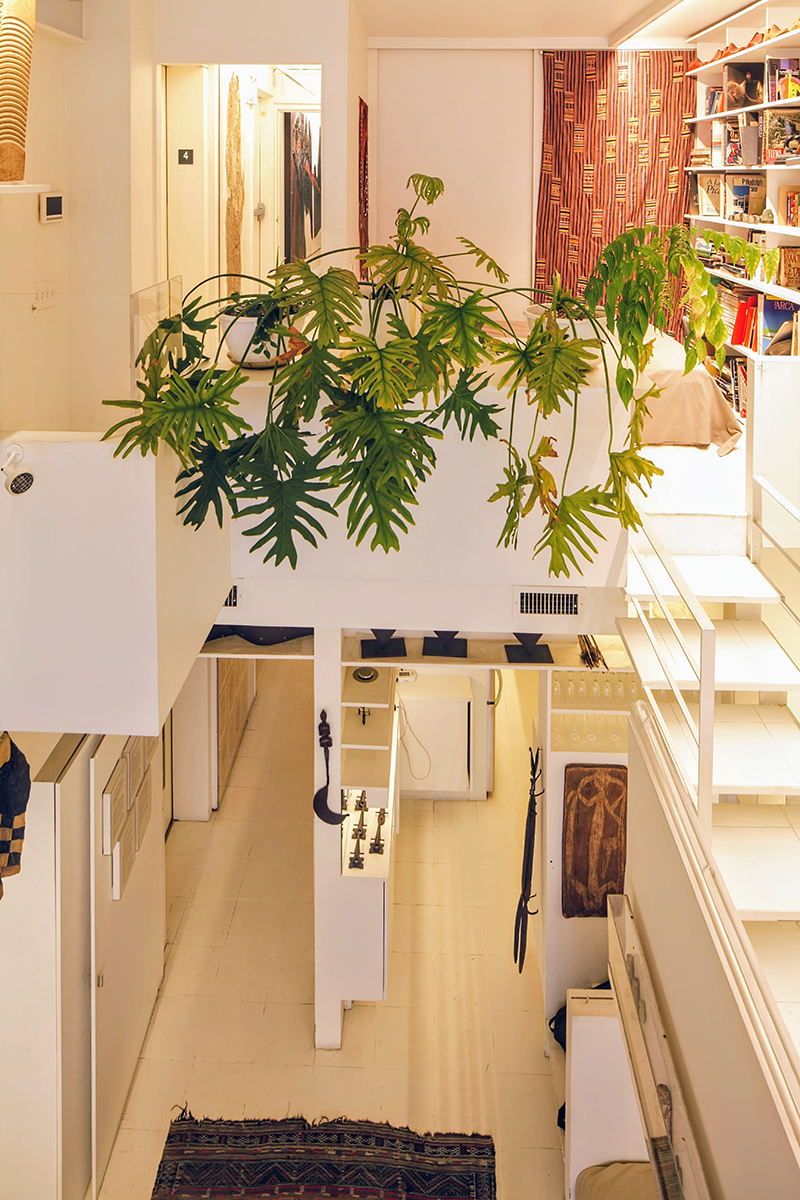 Image of apartment interior looking down from balcony to the floor below. Walls and furniture are largely white, as is staircase on the right side of photo.