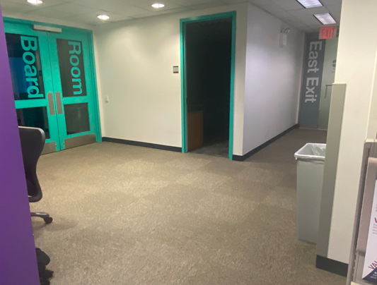 There are two entrances to the conference room. The entrances are turquoise. The conference room entrance on the left has two doors with glass windows with the words Board Room painted on it. The conference room entrance door on the right is open. The East Exit is also shown here.