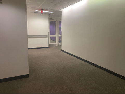 This is a hallway with white walls that leads from the elevator to the  MOCS' main entrance that has two doors with glass windows.