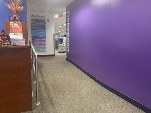 There is a purple wall with the word Reception painted in white letters and the ramp that leads from the reception area into the office. The ramp has a handrail on the left side.
