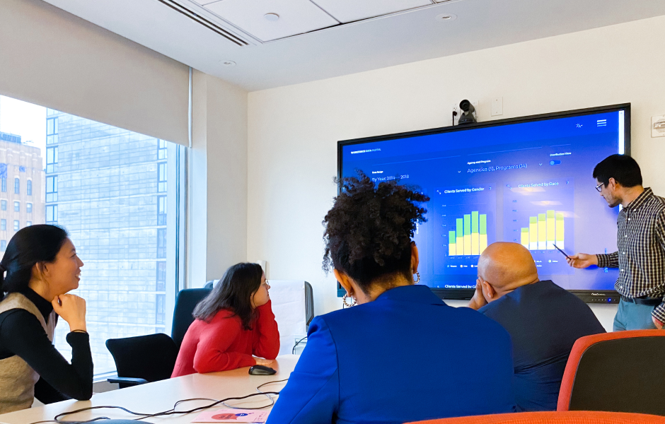 Group of coworkers in a conference room reviewing workforce data and graphs on a large screen