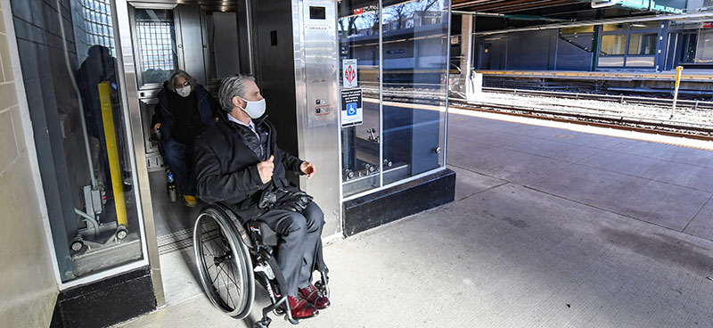 Two people in wheelchairs moving from an elevator to a transit station