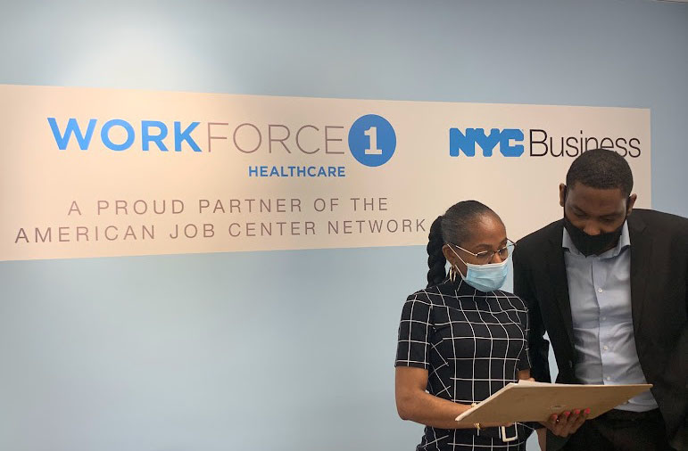woman and man wearing masks looking at paperwork standing in front of sign that has Workforce1 and NYC Business logos