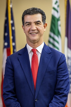 Portrait of NYC DOT Commissioner Ydanis Rodriguez. He is wearing a blue suit with a white shirt and red tie.