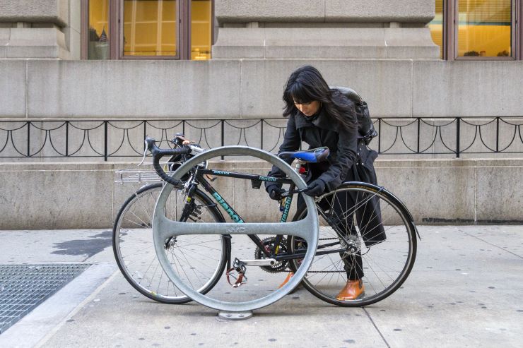 A woman secures her bicycle on a round bike rack in the sidewalk