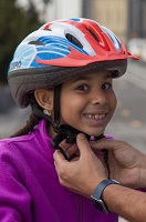 A young boy smiles as someone put a bicycle helmet on his head.