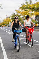 Two women ride colorful bikes on a bike lane.