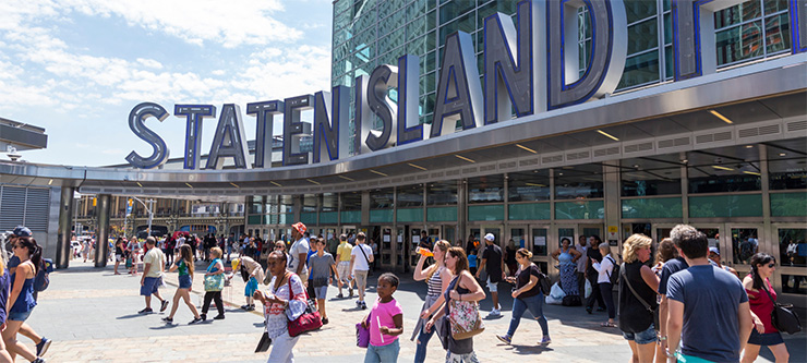  People walk out of the Staten Island Ferry terminal on a sunny day.