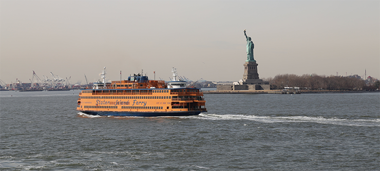 An orange Staten Island Ferry travels in the New York Harbor past the Statue of Liberty