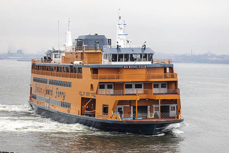 A large, orange Staten Island Ferry named for S.S.G. Michael H. Ollis travels in the New York Harbor