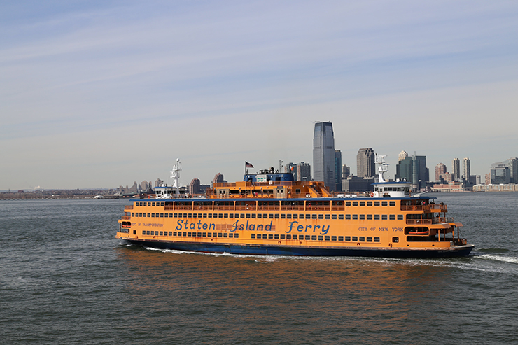 An orange Staten Island Ferry named for John J. Marchi travels in the New York harbor.