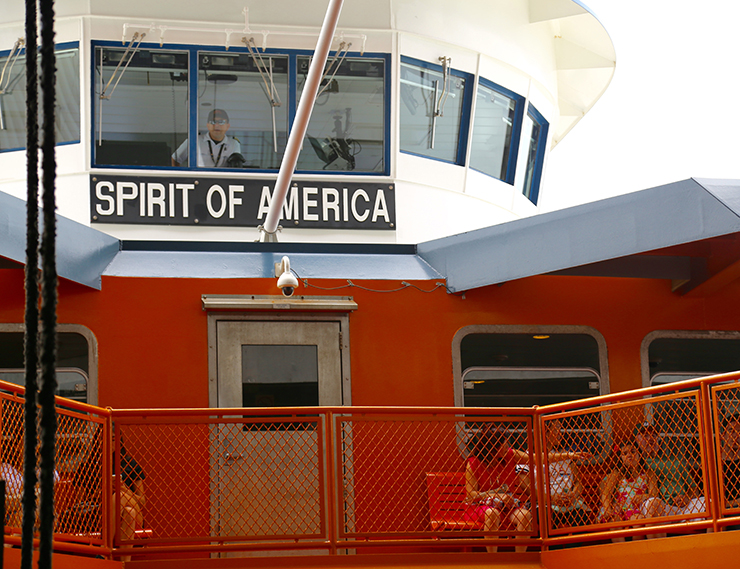 People sit on an orange ferry, under near the ferry's name: Spirt of America.