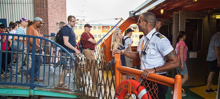 A crew member welcomes passengers boarding a ferry.