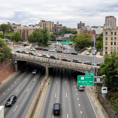 Overview of an expressway with six lanes of moving vehicles and overpass with parked cars and two lanes of traffic traveling over the expressway.