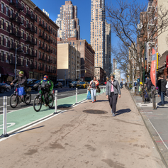 Pedestrians walk on an extended sidewalk next to a green bike lane.