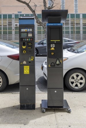 Side by side image of a Pay-And-Display meter and Pay-By-Plate Meter. The Pay-By-Plate has a touch screen and larger solar panel.