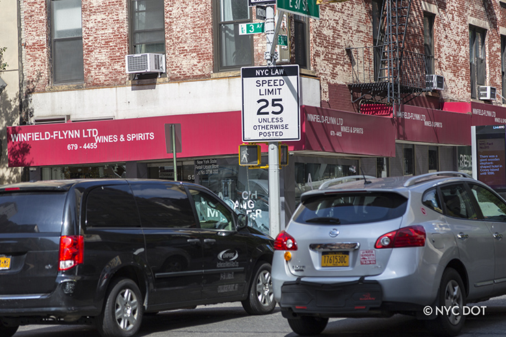 Cars travel along an avenue in NYC, driving past a sign that reads: NYC Law Speed Limit 25 unless otherwise posted.