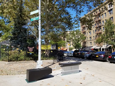 A metal sculptural bench designed to mimic a hair comb installed on a wide sidewalk