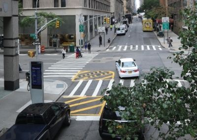 A car turns left around a slow turn wedge treatment with yellow markings and rubber speed bumps near the corner of the intersection. The driver slows down, turns wide, and sees pedestrians in the crosswalk before completing their turn.