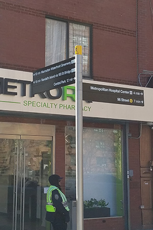 Directional signs are posted on the top of a narrow pole, positioned in front of a business in NYC