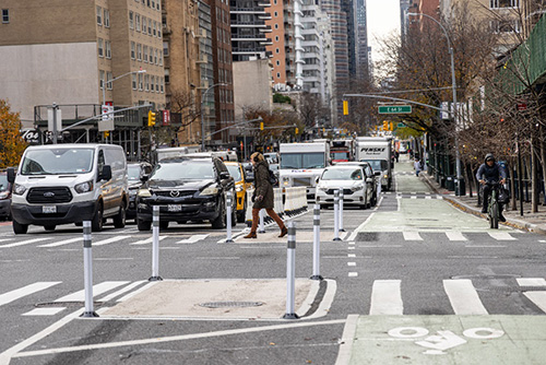 Cars and cyclists wait at an intersection while a pedestrian crosses Third Avenue in Manhattan. 